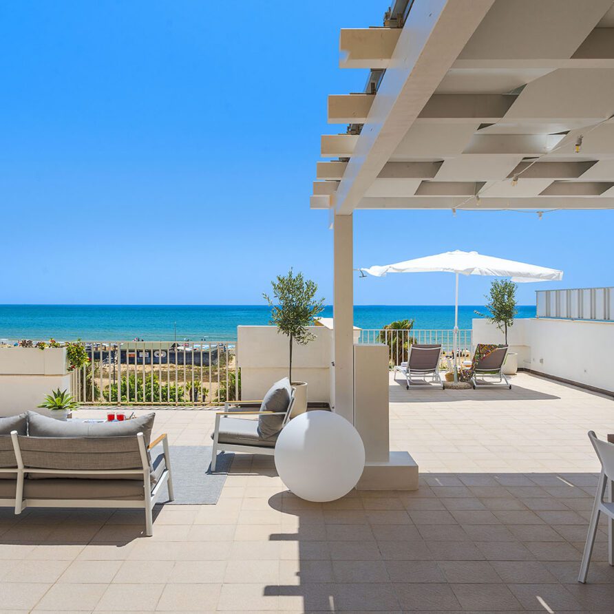 Terrazza panoramica con sedie, ombrelloni e vista sul mare e spiaggia in una giornata soleggiata