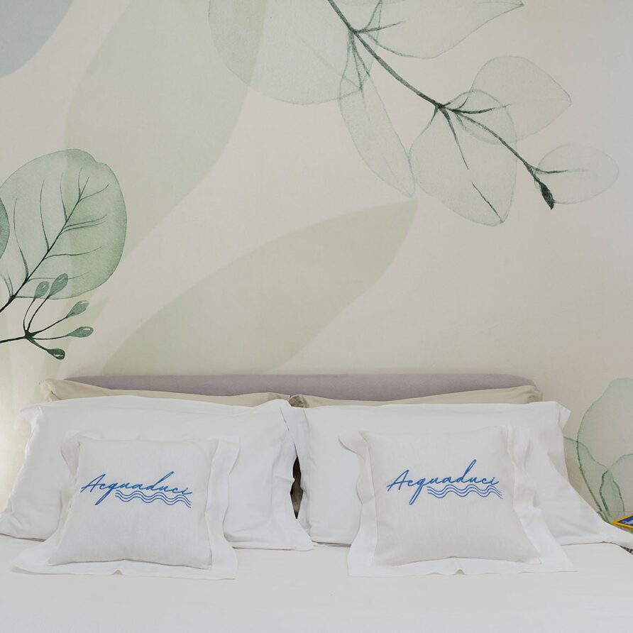 Letto con cuscini bianchi con dettagli blu e decorazioni floreali murali delicate e luminose