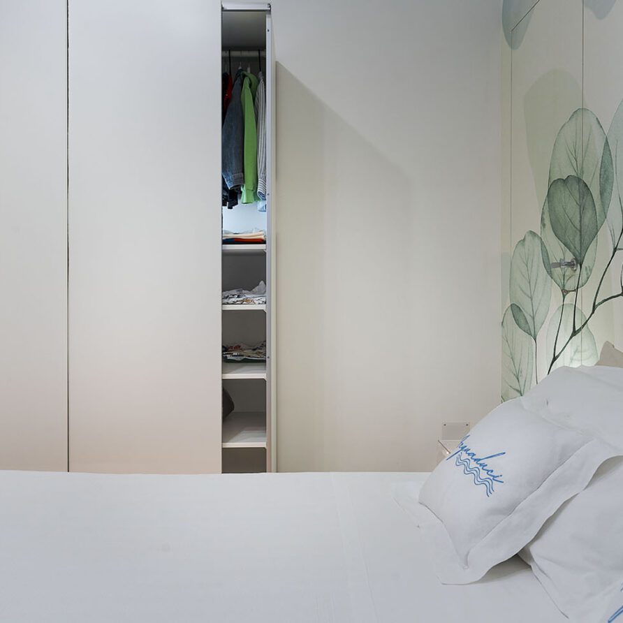 Vista di una camera da letto con parete decorativa con foglie verdi e armadio bianco aperto