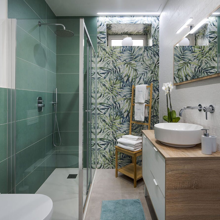 Bagno moderno con pareti in piastrelle verdi, lavabo su mobile di legno e specchio grande sopra il lavandino