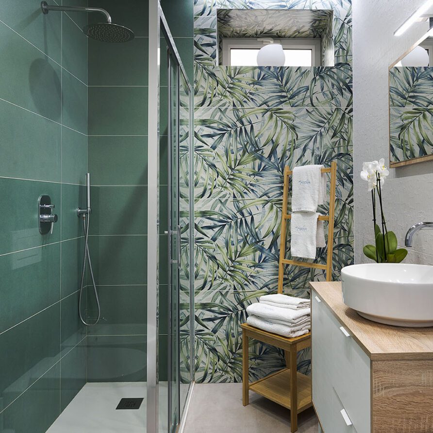 Bagno moderno con piastrelle verdi e decorazione floreale sulla parete della doccia, lavabo bianco e accessori di design