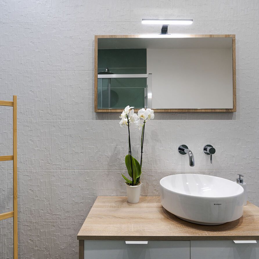 Lavabo rotondo bianco sopra un piano in legno con specchio e fiore di orchidea sullo sfondo