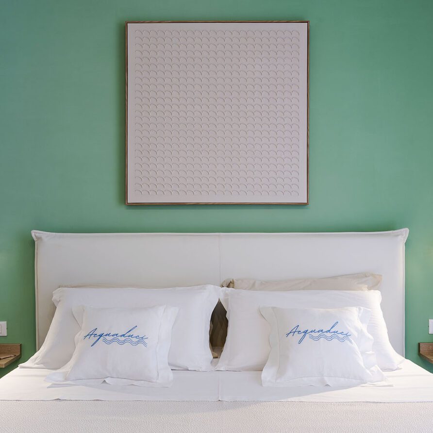 Camera da letto moderna con parete verde, letto matrimoniale con cuscini e lampade da lettura ai lati