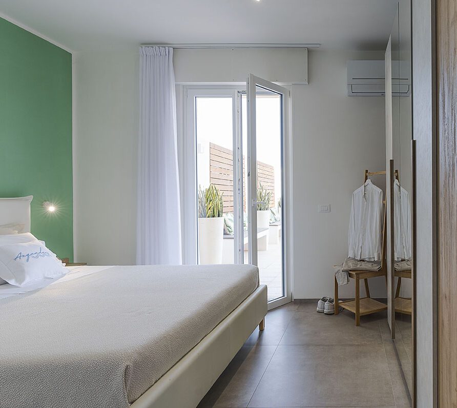 Camera da letto moderna con parete verde, letto matrimoniale, finestra con tende e balcone, arredi eleganti e decorazioni minimaliste
