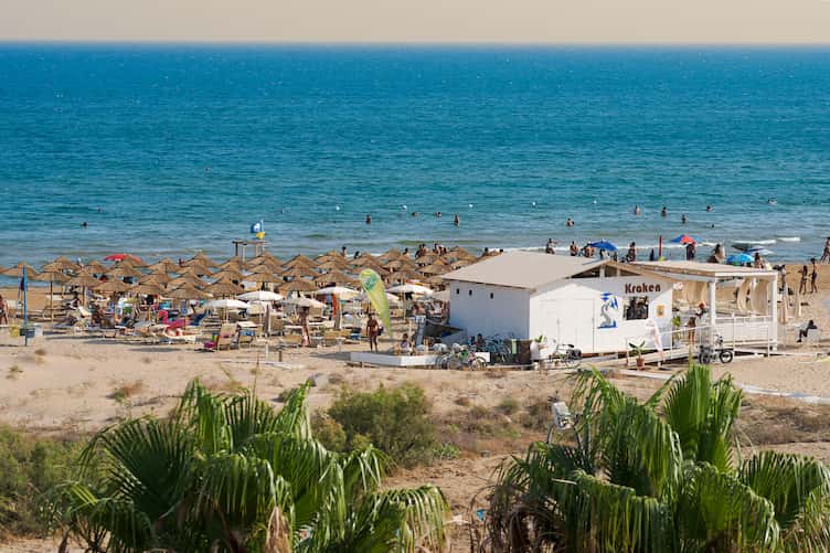 Spiaggia con ombrelloni, turisti e mare blu, scena vivace sulla costa di una località balneare