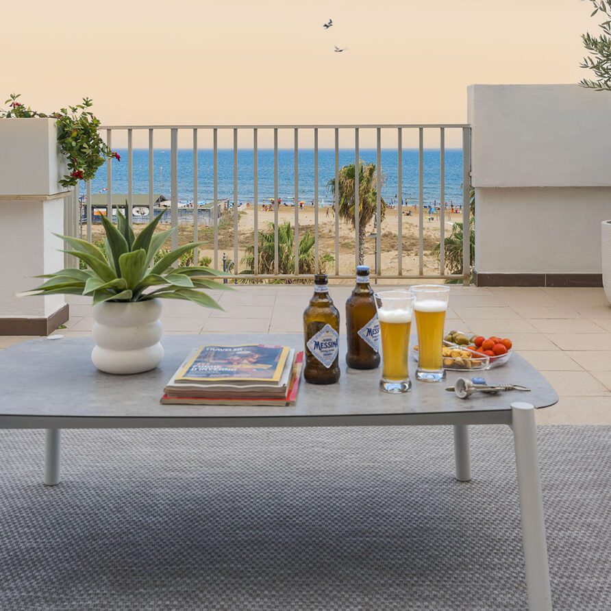 Tavolo da esterno con bevande, riviste e snack su una terrazza con vista mare e arredi minimalisti