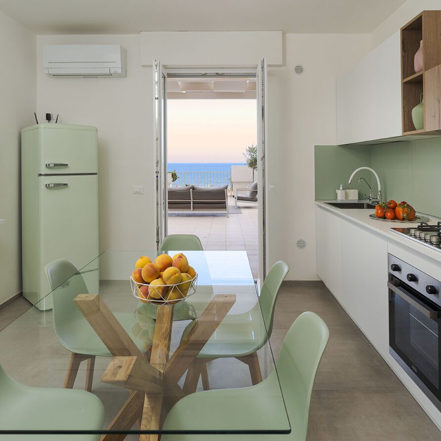 Cucina moderna e luminosa con tavolo da pranzo, frigorifero e vista sul mare attraverso la finestra