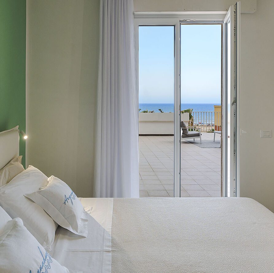 Camera da letto luminosa con vista sul mare e accesso a un balcone con sedie all'aperto