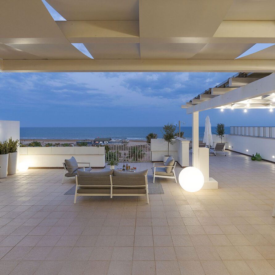 Terrazza moderna con vista mare, sedie e tavolini per relax, illuminazione soffusa e arredamento elegante