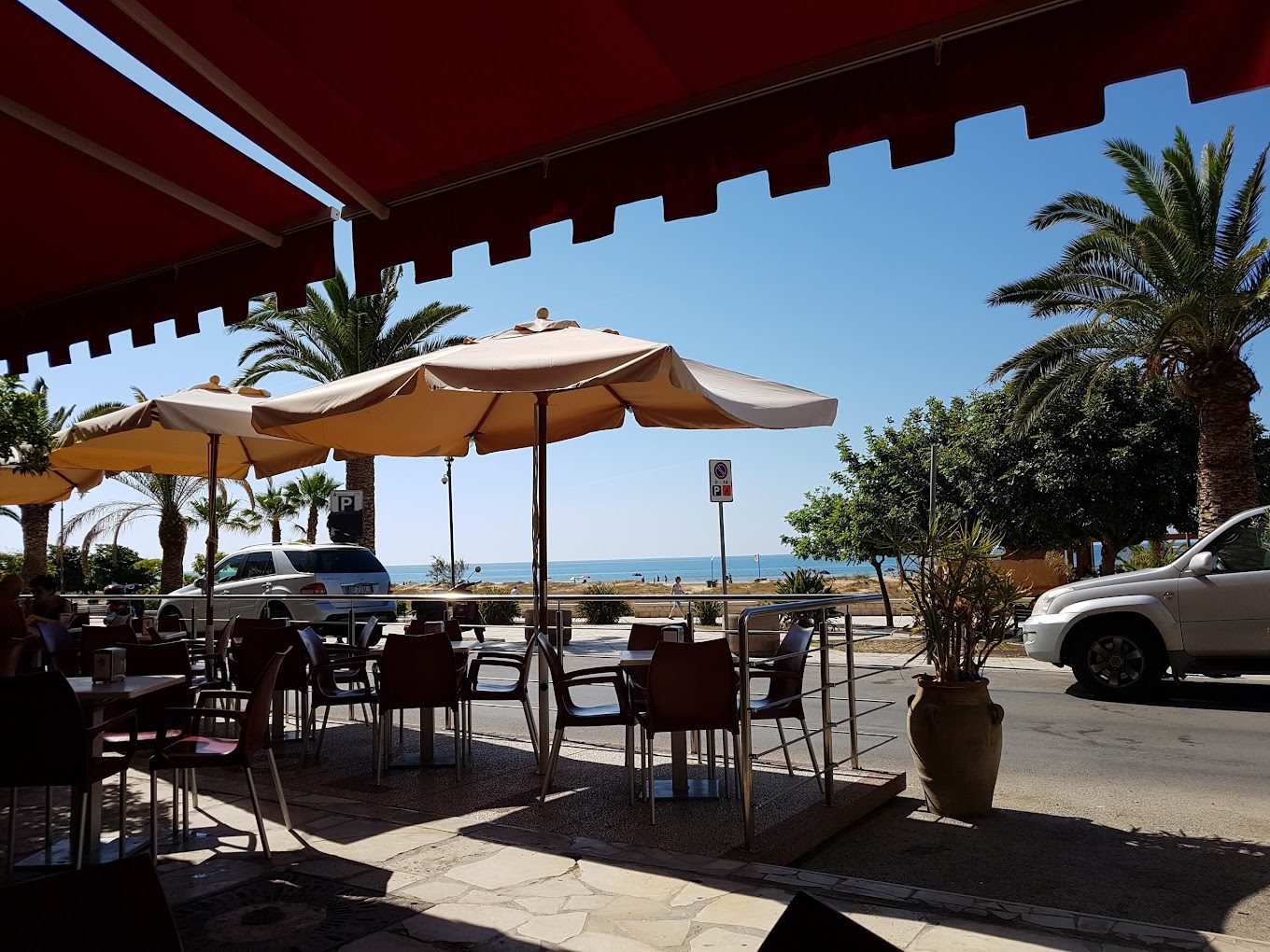 Terrazza di ristorante con ombrelloni e vista sul mare, tavoli all'aperto sotto un sole estivo