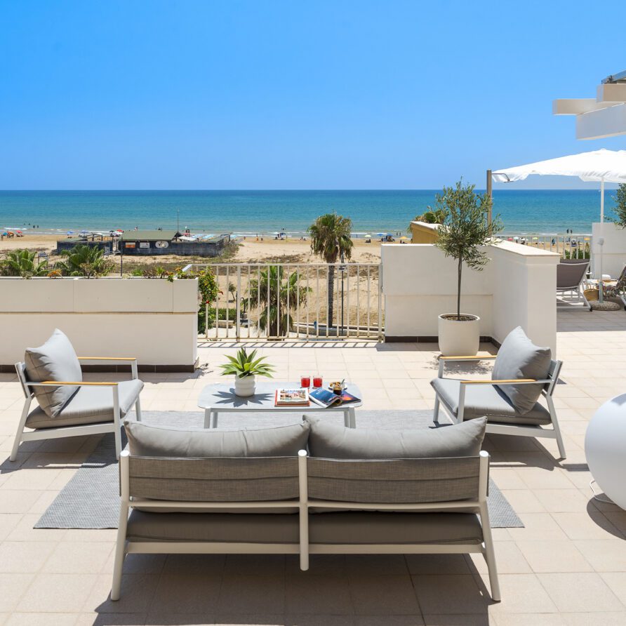 Terrazza vista mare con mobili da esterno e ombrellone, panorama spiaggia e cielo blu