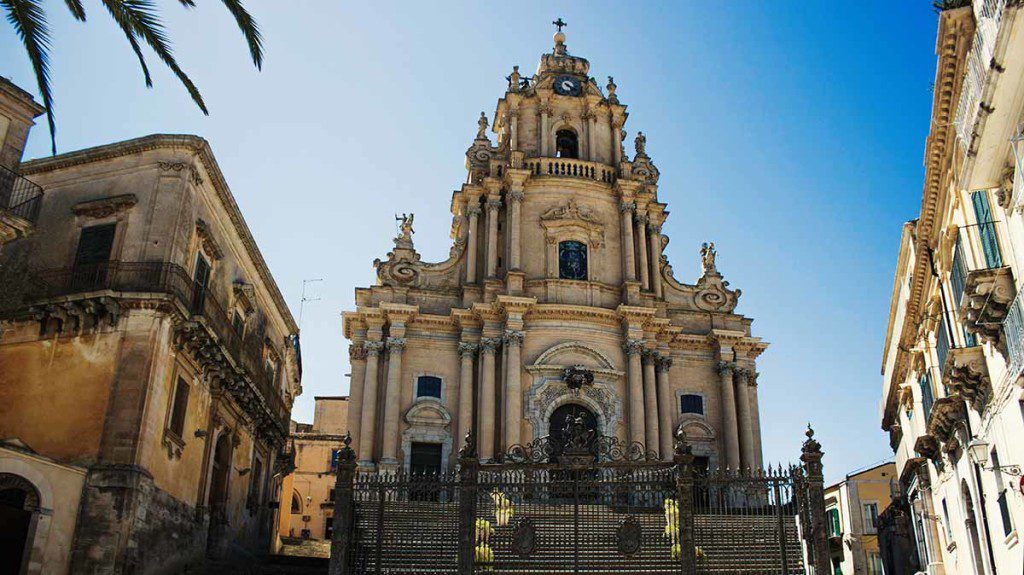 Chiesa barocca storica con facciata ornata e torre imponente, situata in una piazza affollata di una città spagnola