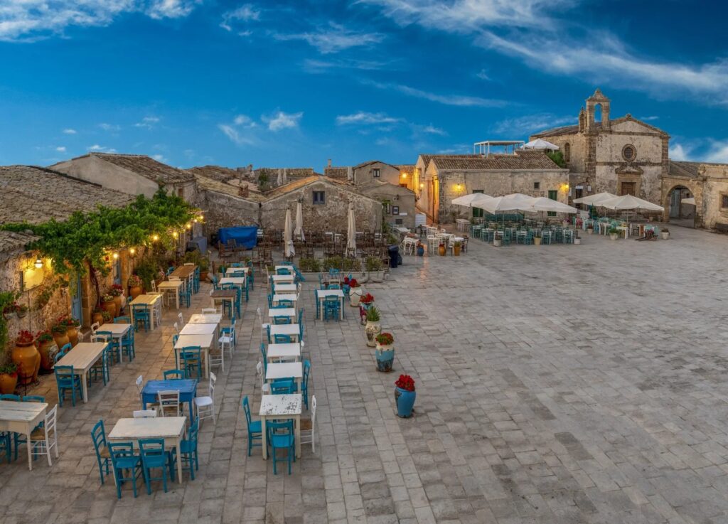 Spiaggia di sassi con tavoli e sedie vicino a un edificio storico in un comune di mare durante il tramonto