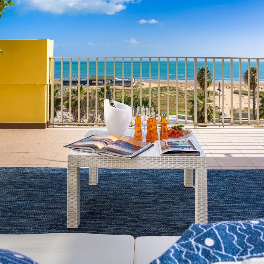 Terrazza con tavolino con bevande e riviste, vista panoramica sul mare e sulla costa di giorno