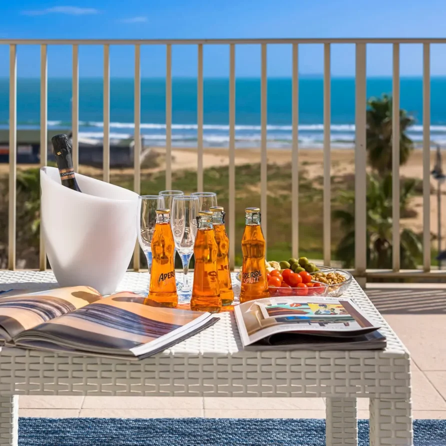 Balcone con tavolino vista mare, assorbenti, libro, e bevande estive in una giornata soleggiata