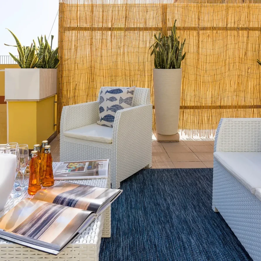 Zona lounge all'aperto con mobili in vimini, cuscini colorati, piante in vasi e decorazioni in stile estivo