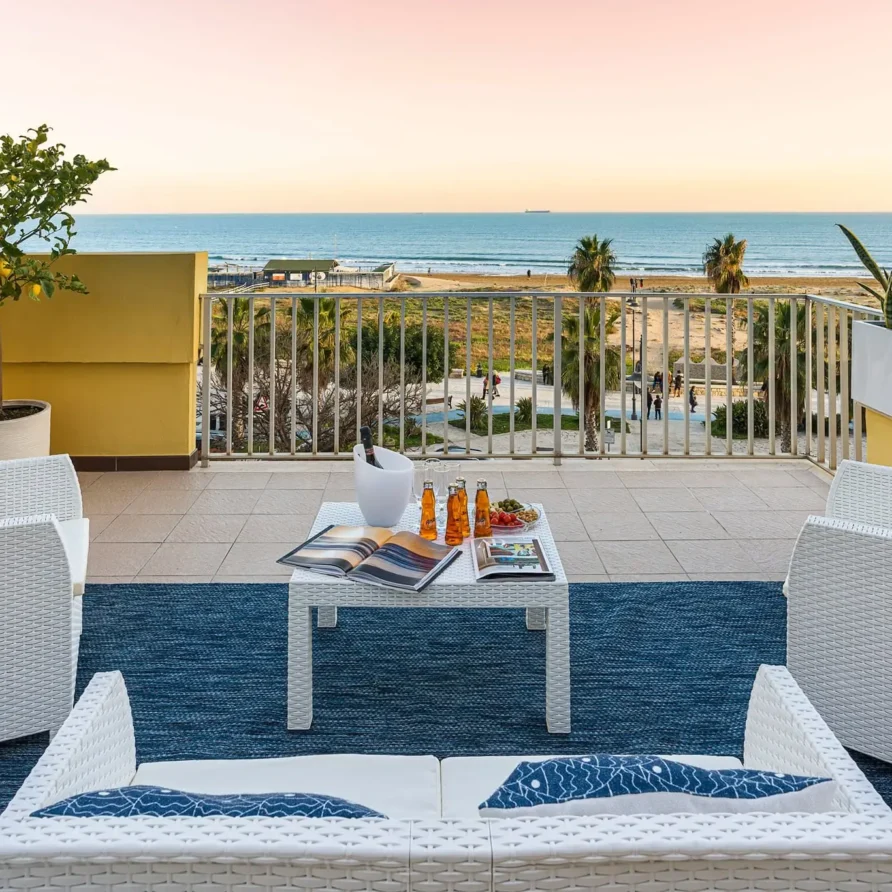 Terrazza con vista sul mare, sedie in vimini bianche, palme e paesaggio marino al tramonto