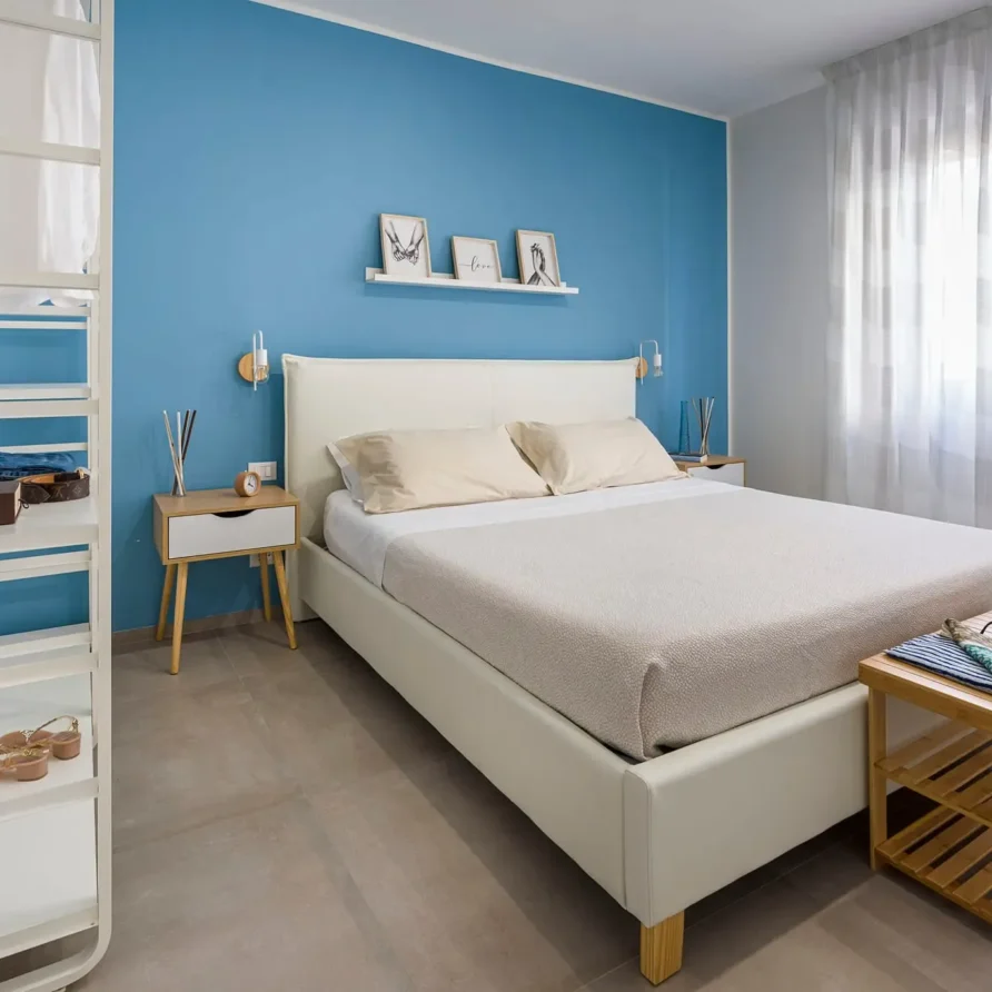 Camera da letto luminosa con pareti azzurre, letto bianco, tende leggere e arredamento minimalista