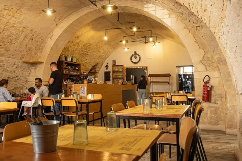 Interno di un ristorante con arredi in stile rustico, tavoli e sedie, clienti seduti e personale che serve