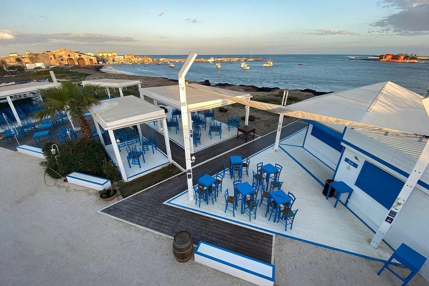 Terrazza fronte mare con area lounge, tavoli e sedie in stile mediterraneo con vista sull'oceano e il cielo sereno