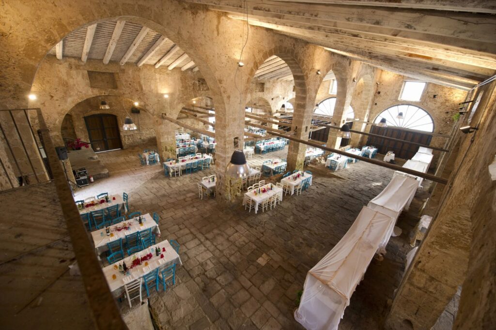 Interno di una storica sala di ricevimento con tavoli decorati e archi in pietra, ideale per eventi e matrimoni