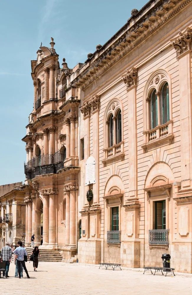 Esterno di un imponente edificio in stile barocco con dettagli decorativi e finestre arcuate, sotto un cielo blu