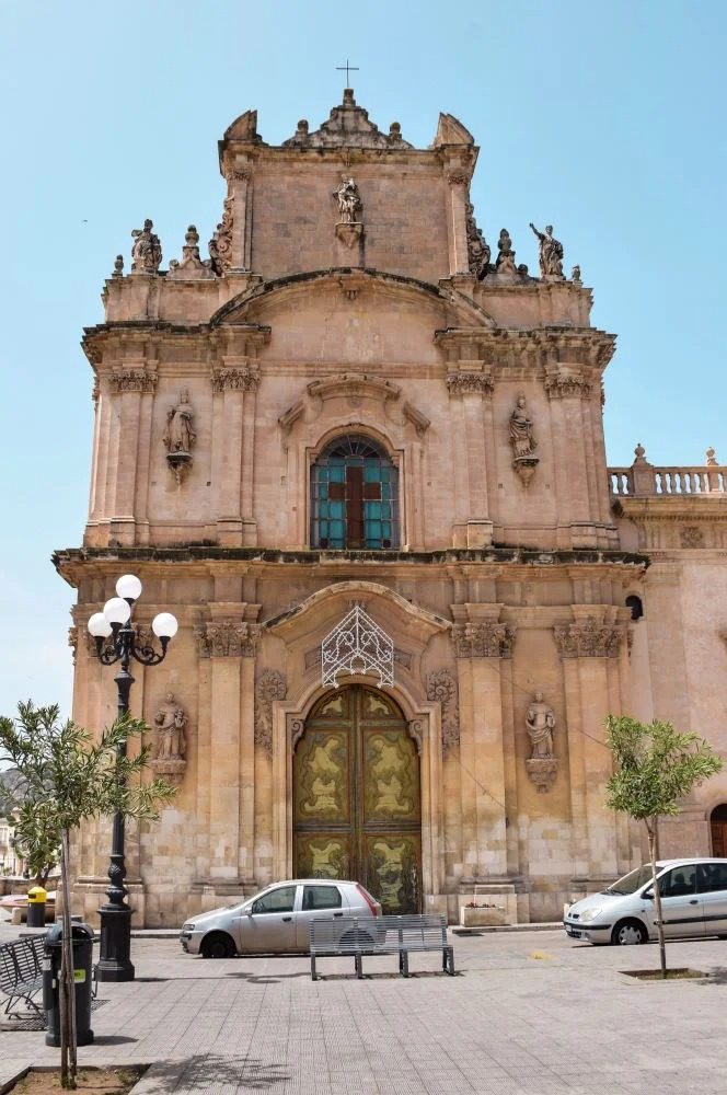 Facciata storica di un edificio barocco con dettagli decorativi e una portale centrale al centro di una piazza pubblica