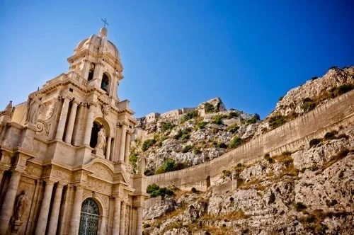 Facciata di una chiesa storica immersa in un paesaggio roccioso sotto un cielo celeste
