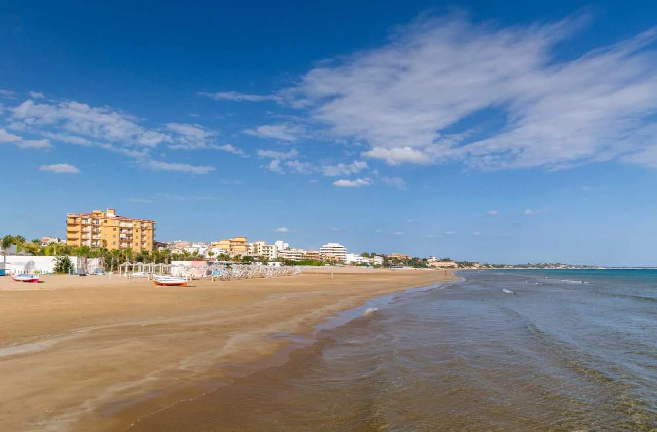 Spiaggia di sabbia con mare calmo e città sullo sfondo sotto un cielo sereno