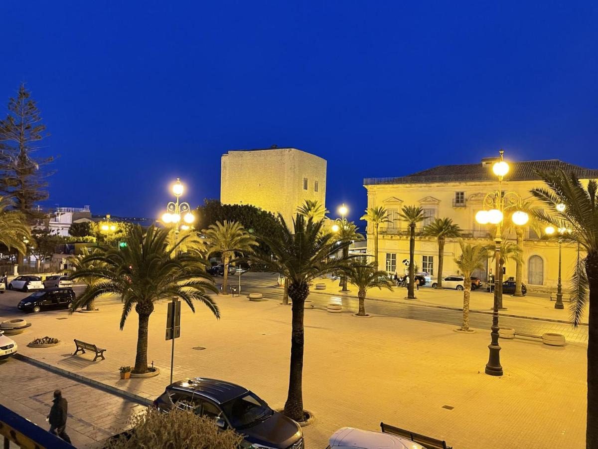 Luogo pubblico con palme, lampioni e edifici storici illuminati di sera in Italia