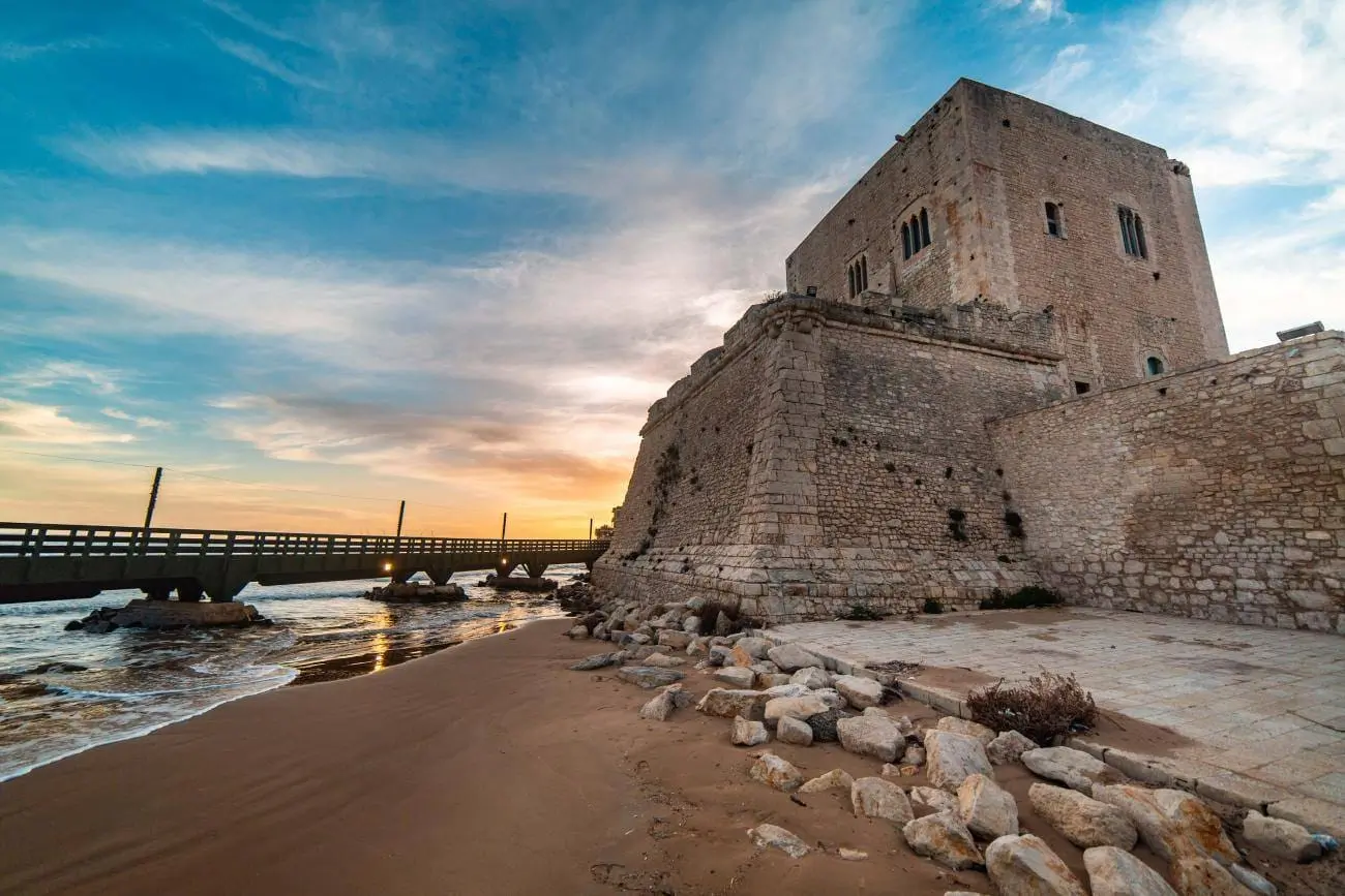 Castello storico situato sulla spiaggia con mare al tramonto e cielo nuvoloso
